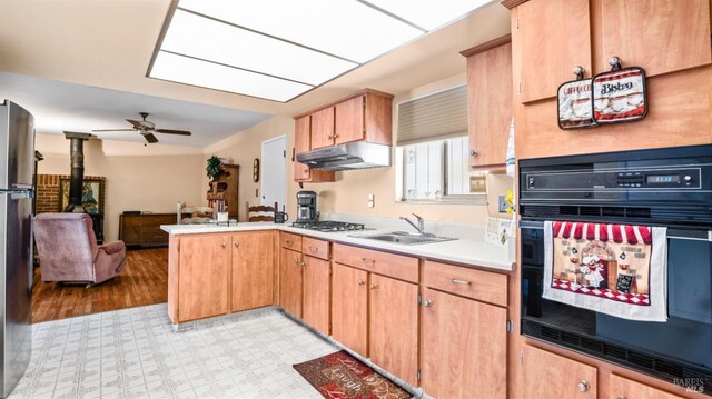 kitchen with kitchen peninsula, stainless steel appliances, ceiling fan, sink, and a wood stove