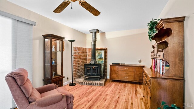 living area featuring ceiling fan, light hardwood / wood-style floors, and a wood stove