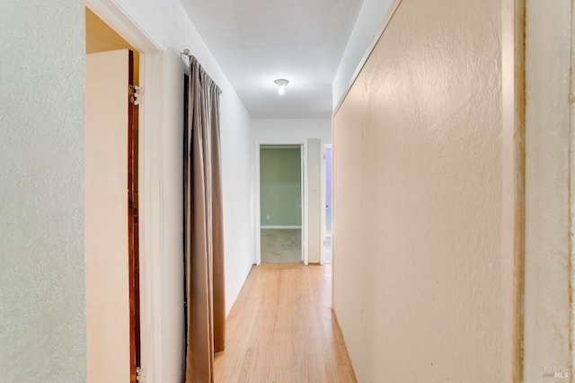 hallway featuring light wood-style flooring and a textured wall