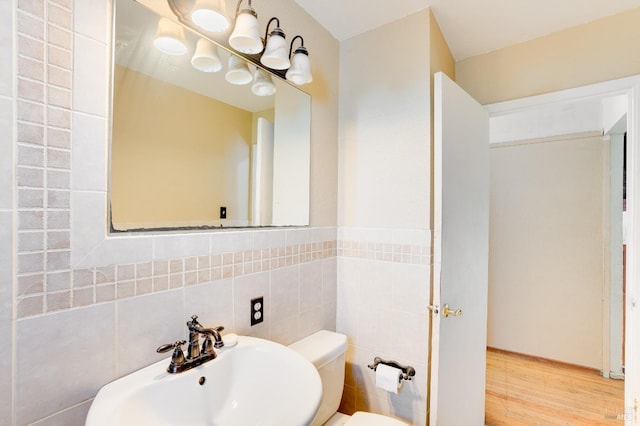 bathroom with toilet, a notable chandelier, wood finished floors, a sink, and tile walls