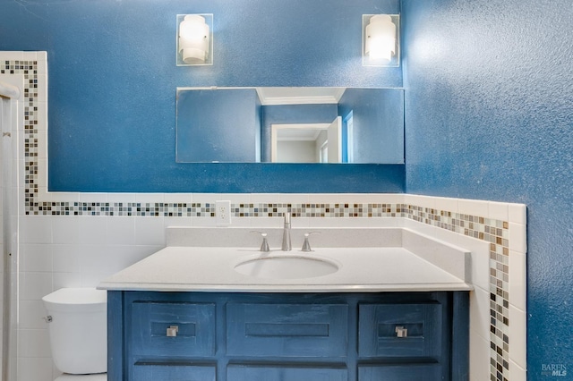 bathroom featuring toilet, a textured wall, and vanity