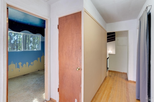 hall with baseboards, an upstairs landing, visible vents, and light wood-style floors