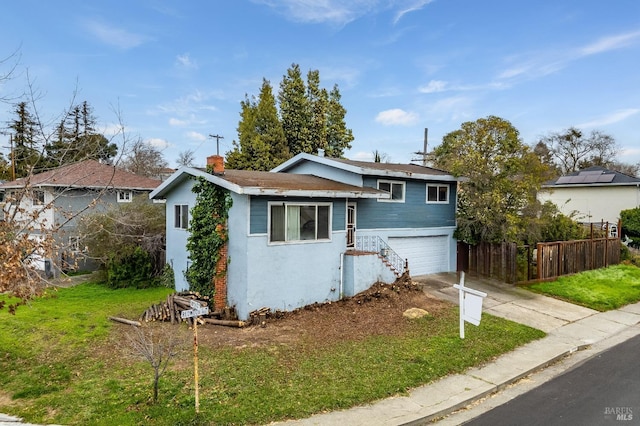 split level home with a chimney, concrete driveway, fence, a garage, and a front lawn