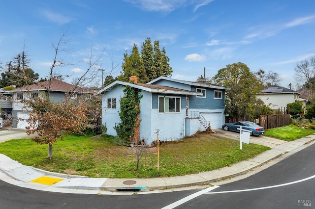 split level home with stucco siding, fence, a garage, driveway, and a front lawn