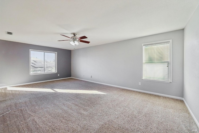 spare room with carpet floors, visible vents, ceiling fan, and baseboards