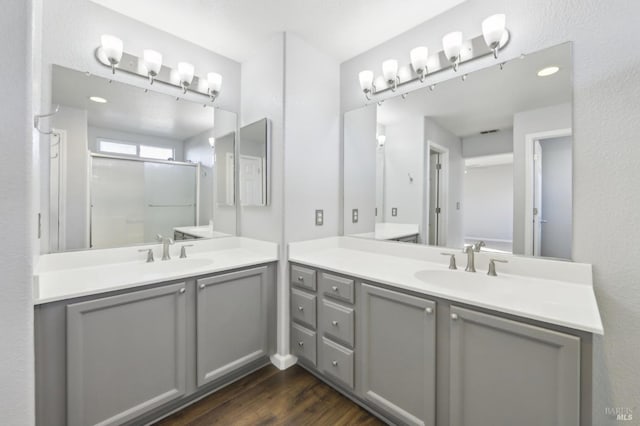 full bath with wood finished floors, a stall shower, two vanities, and a sink