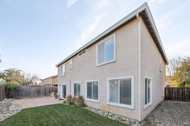 rear view of house with stucco siding, a fenced backyard, a lawn, and a patio