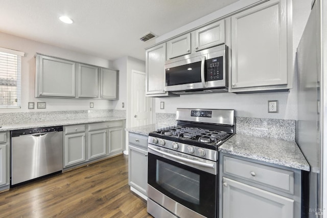 kitchen with visible vents, appliances with stainless steel finishes, dark wood-type flooring, light stone countertops, and gray cabinets