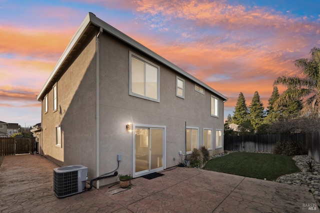 back of property at dusk with central air condition unit, a fenced backyard, a lawn, and a patio