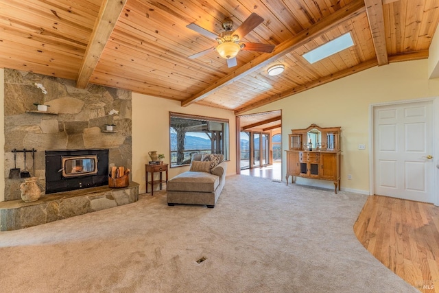 living area with carpet, ceiling fan, a wood stove, and lofted ceiling with skylight