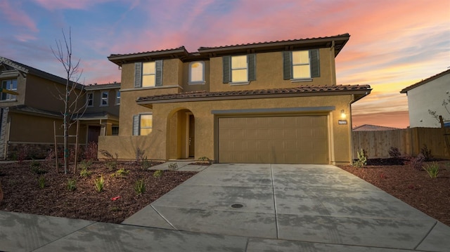 mediterranean / spanish-style house featuring a garage, concrete driveway, a tile roof, fence, and stucco siding