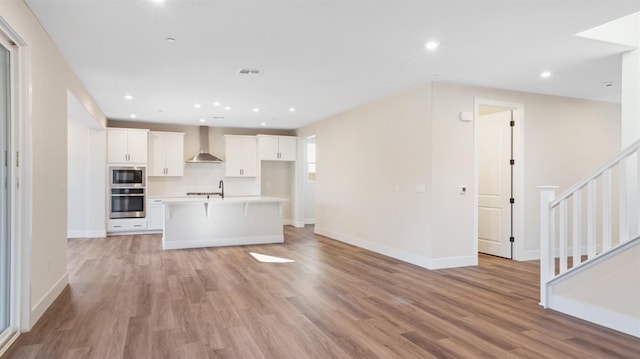 unfurnished living room with light wood-style flooring, recessed lighting, visible vents, baseboards, and stairway