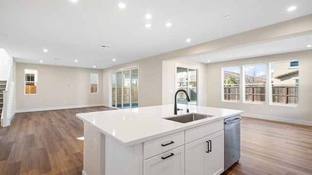 kitchen featuring stainless steel dishwasher, a kitchen island with sink, open floor plan, and a sink