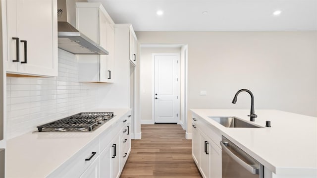 kitchen with stainless steel appliances, light countertops, a sink, and wall chimney exhaust hood