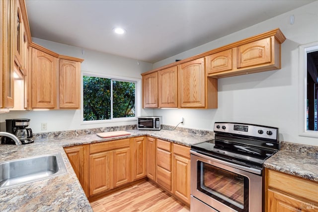 kitchen featuring light stone countertops, stainless steel range with electric cooktop, light brown cabinets, sink, and light wood-type flooring