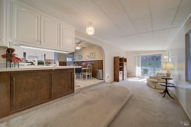 kitchen featuring ceiling fan, light colored carpet, wooden walls, and white cabinetry