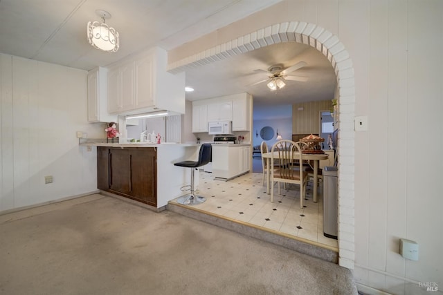 kitchen with wooden walls, ceiling fan, decorative light fixtures, range, and white cabinets