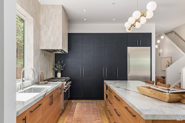 kitchen with light stone countertops, hanging light fixtures, premium appliances, light hardwood / wood-style floors, and sink