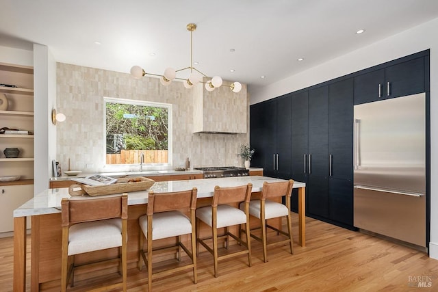 kitchen with decorative light fixtures, light hardwood / wood-style floors, built in fridge, a kitchen breakfast bar, and sink