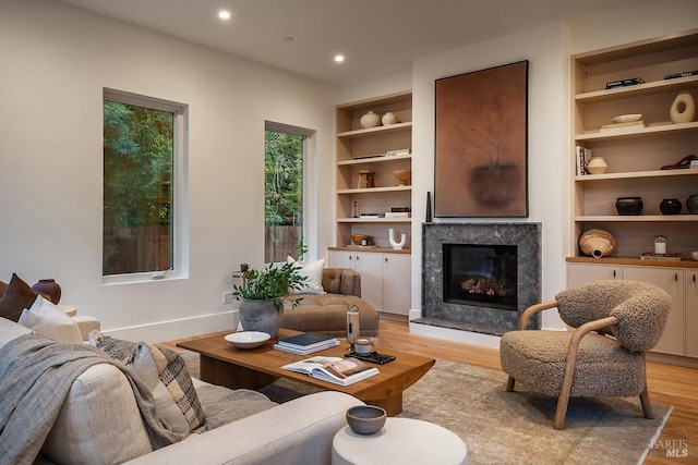 living room with a premium fireplace, built in features, and light hardwood / wood-style flooring