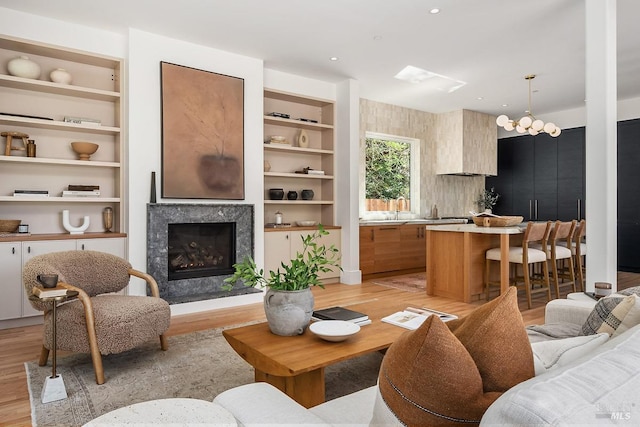 living room featuring a fireplace, built in shelves, light hardwood / wood-style flooring, and sink