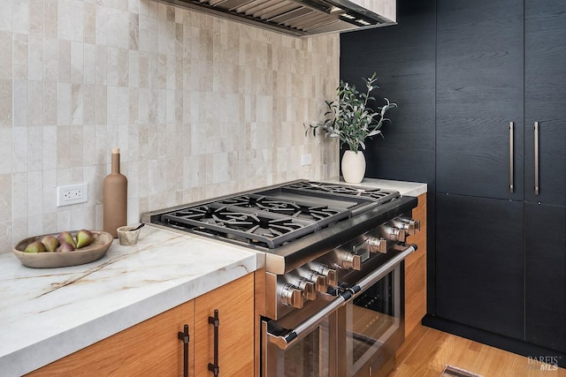 kitchen with light hardwood / wood-style floors, light stone countertops, double oven range, wall chimney exhaust hood, and backsplash