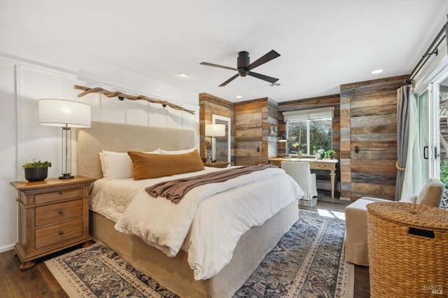 bedroom featuring ceiling fan, dark hardwood / wood-style flooring, access to outside, and wooden walls