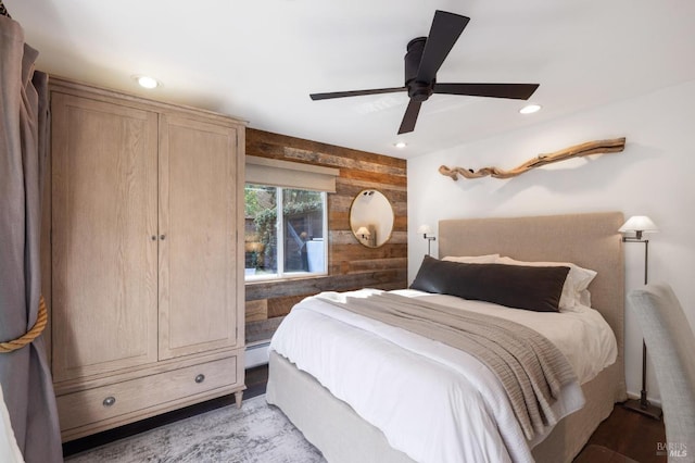 bedroom with ceiling fan, a baseboard heating unit, and wooden walls