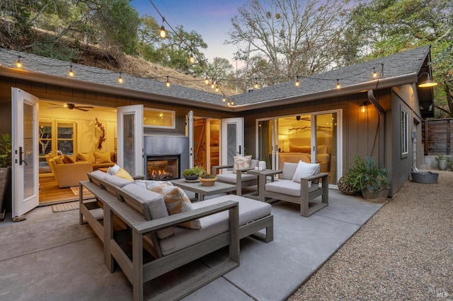 back house at dusk featuring a patio and an outdoor living space with a fireplace