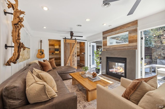 living room with ceiling fan, a barn door, a large fireplace, and a wealth of natural light