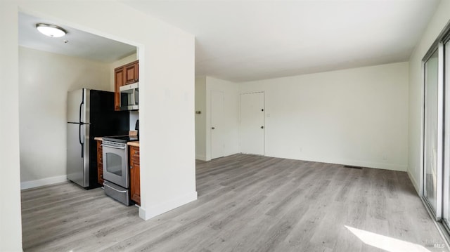kitchen with brown cabinets, light countertops, light wood-type flooring, baseboards, and appliances with stainless steel finishes