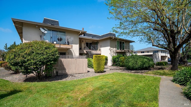 back of house featuring stucco siding, fence, a balcony, and a lawn