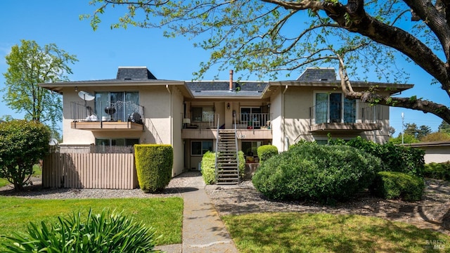 view of front of property featuring roof with shingles, fence, stairway, a balcony, and stucco siding