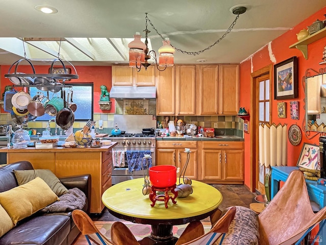 kitchen featuring under cabinet range hood, tile countertops, an inviting chandelier, decorative backsplash, and high end range