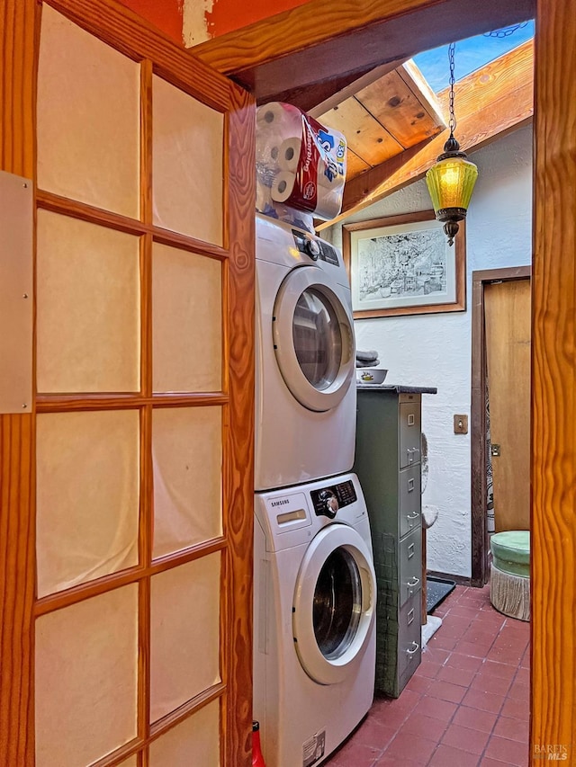 laundry room featuring dark tile patterned flooring and stacked washing maching and dryer