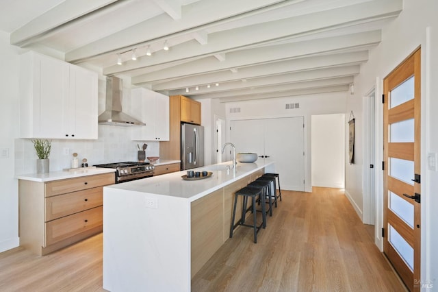 kitchen featuring appliances with stainless steel finishes, beamed ceiling, wall chimney exhaust hood, and a kitchen bar