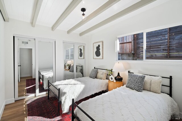 bedroom with beam ceiling, french doors, multiple closets, and hardwood / wood-style flooring