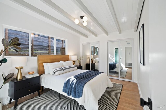 bedroom featuring two closets, light hardwood / wood-style flooring, and beamed ceiling