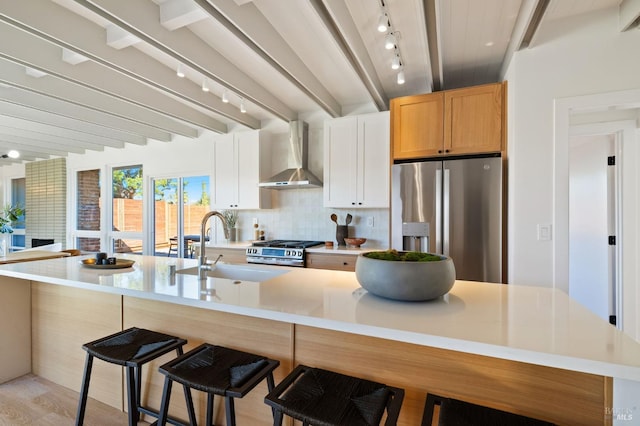 kitchen with stainless steel appliances, a sink, beam ceiling, wall chimney exhaust hood, and tasteful backsplash