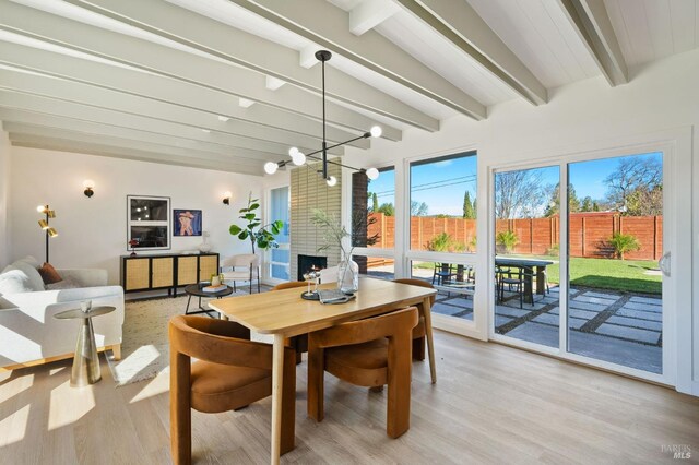 dining room with a fireplace, light wood-type flooring, a notable chandelier, and beam ceiling