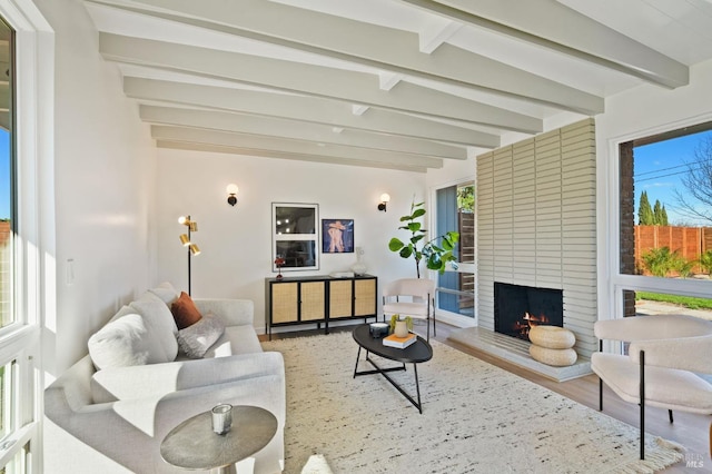 living area with a large fireplace, beamed ceiling, and wood finished floors