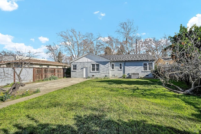 rear view of property featuring a lawn, concrete block siding, and fence