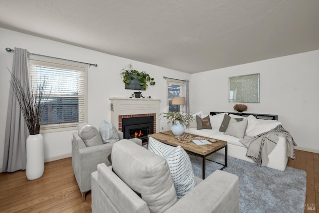 living room with a brick fireplace, light wood-style flooring, and baseboards