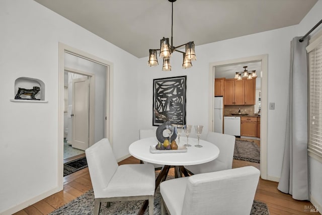 dining space featuring a chandelier, light wood-type flooring, and baseboards