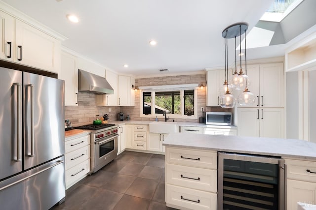 kitchen featuring decorative light fixtures, white cabinetry, high end appliances, beverage cooler, and wall chimney range hood