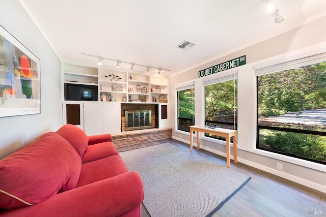 living room with built in features, wood-type flooring, and a stone fireplace