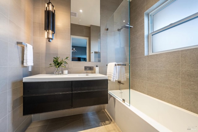 bathroom with bath / shower combo with glass door, tile patterned flooring, vanity, and tile walls