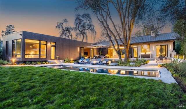 back house at dusk with a patio area and a lawn