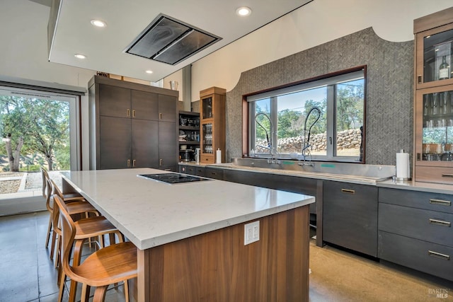 kitchen featuring black electric stovetop, a kitchen island, a wealth of natural light, and a kitchen breakfast bar