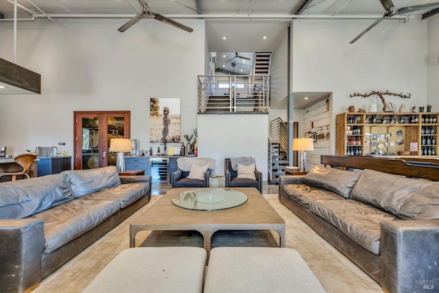 living area with a towering ceiling, ceiling fan, wine cooler, and stairway